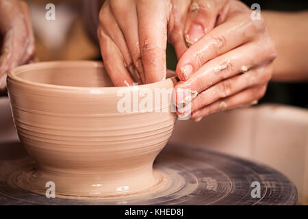 Un close-up della donna potter insegna la pupilla come fare una ciotola profonda di argilla su un tornio del vasaio in officina Foto Stock