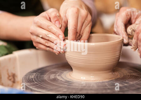 Un close-up della donna potter insegna la pupilla come fare una ciotola profonda di argilla su un tornio del vasaio in officina Foto Stock