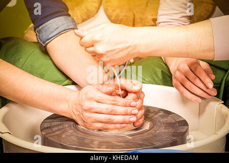 Close-up donna potter insegna l'allievo per effettuare correttamente una ciotola profonda di argilla su un tornio del vasaio e in aggiunta acqua la creta con acqua. formazione Foto Stock