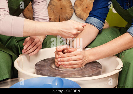 Close-up donna potter insegna l'allievo per effettuare correttamente una ciotola profonda di argilla su un tornio del vasaio e in aggiunta acqua la creta con acqua. formazione Foto Stock