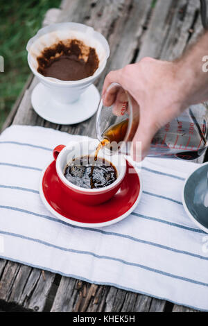 Delizioso preparato di fresco outdoor versare il caffè versando in rosso di porcellana tazza da caffè Foto Stock