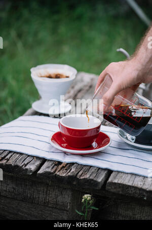 Delizioso preparato di fresco outdoor versare il caffè versando in rosso di porcellana tazza da caffè Foto Stock