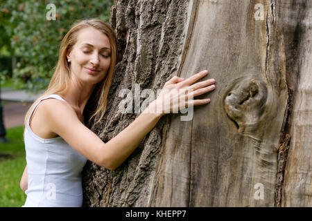 Giovane donna abbracciando grande albero Foto Stock