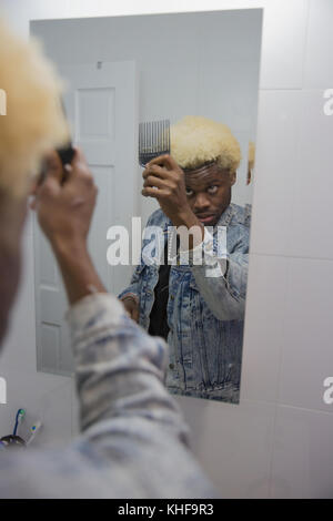 Giovane uomo utilizza un capello pick a pettinare i capelli in specchio Foto Stock