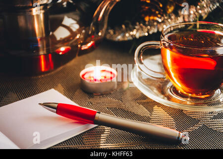 Aperto il blocco note con la penna sul tavolo vicino calda tazza di tè nero Foto Stock