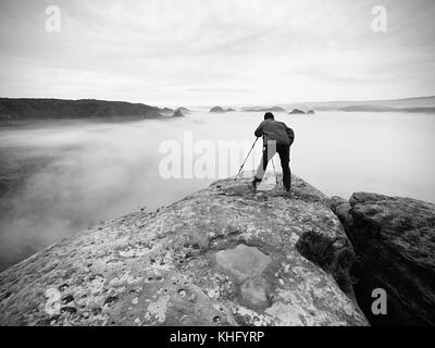 Fotografo sul cratere. l uomo sul picco sopra nube spessa, scuro tempo piovoso nel sentiero di montagna. Foto Stock