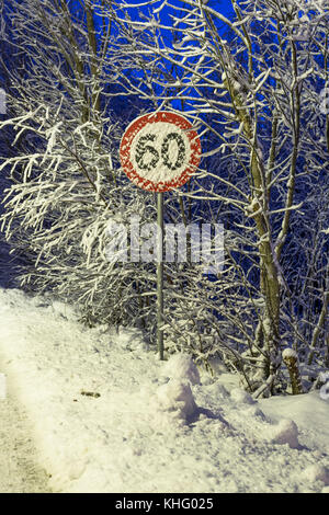 Inizio sera d'inverno con neve, 60 km/t cartello stradale coperto di neve Foto Stock