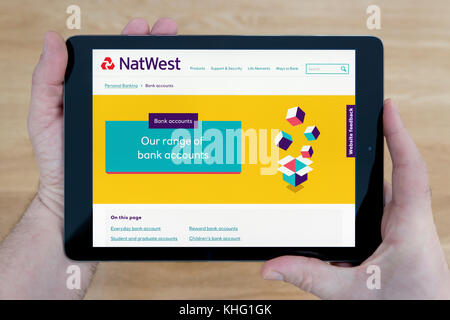 Un uomo guarda la Natwest Bank sito sul suo iPad dispositivo tablet, sparato contro un tavolo di legno top sfondo (solo uso editoriale) Foto Stock
