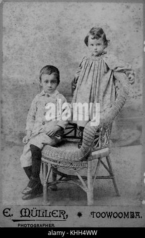 Un ritratto di Toowoomba, datato tra il 1890 e il 1900, che mostra due bambini posati su una sedia di canna. Questa fotografia cattura un momento di vita familiare durante la fine del XIX secolo. Foto Stock
