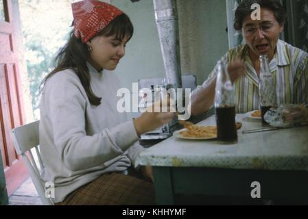 Giovane ragazza che indossa bandana rossa e sorride mentre mangia un pasto e condivide i colas Pepsi con la nonna a un tavolino, 1966. Foto Stock