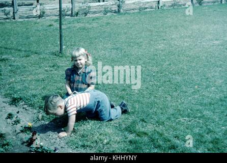 Due bambini, un fratello e una sorella, che giocano in un parco, il ragazzo strisciando verso una fila di fiori, 1952. Foto Stock