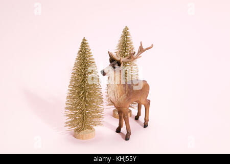 Golden albero di natale con le renne figurina accanto ad esso su un vivace colore rosa sfondo. minimo di vita ancora fotografia Foto Stock