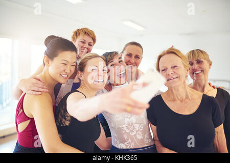 Mescolò età gruppo di donne ridere mentre in piedi insieme prendendo selfies durante le lezioni di ballo in uno studio di danza Foto Stock