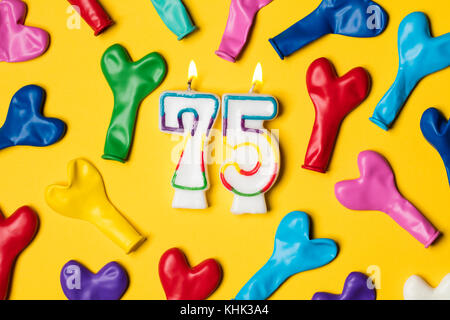Numero 75 candela con palloncini di partito su un brillante sfondo giallo Foto Stock