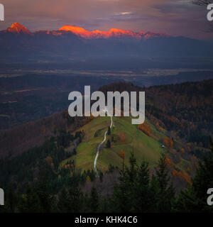 Jamnik, Slovenia - veduta aerea del bel tramonto dorato alla chiesa di San Primoz di Jamnik. Alpi Giulie alla luce del sole Foto Stock