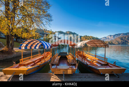 Bled, Slovenia - Barche tradizionali a Pletna rosse, arancioni e blu al sole autunnale sul Lago di Bled Foto Stock