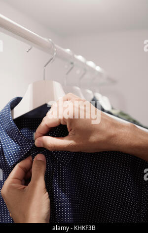 Primo piano di un giovane uomo caucasico serraggio o allentamento dei pulsanti di una camicia appesa sul rack di un armadio Foto Stock