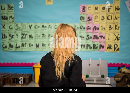 Istruzione secondaria nel Regno Unito: Vista posteriore di una studentessa adolescente giirl di fronte all'elemento tavola periodica sul muro in una lezione di chimica scientifica Foto Stock