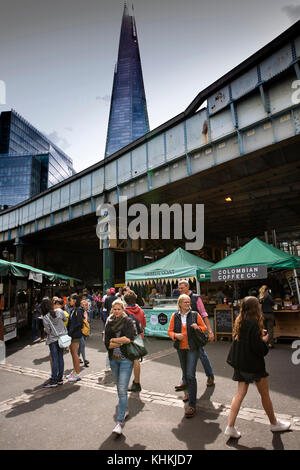 UK, Londra, Southwark, Borough Market, la mattina presto i visitatori in outdoor cibo caldo area al di sotto della linea ferroviaria Foto Stock