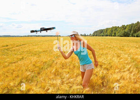 La ragazza bionda nel cappello bianco con un fly swatter allontana drone, contro il campo di grano Foto Stock