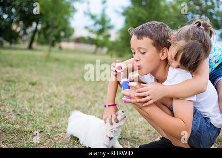 Due giovani fratelli abbracciando l'amicizia e l'amore. carino bambina appoggiata su un dorso di suo fratello mentre sta cercando di soffiare una bolla. Foto Stock