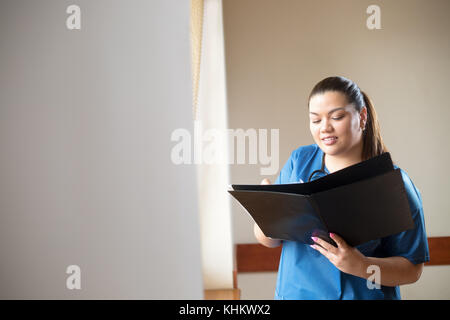 I giovani ispanici medico donna sorridente, tenendo un rapporto e cercando nella cartella lei tiene nelle sue mani Foto Stock