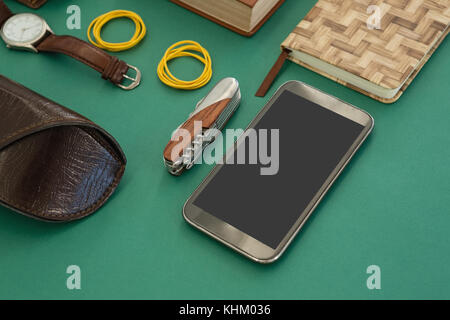 Close-up di agenda, orologio da polso, pocketknife, telefono cellulare e occhiali da sole caso sulla gr Foto Stock