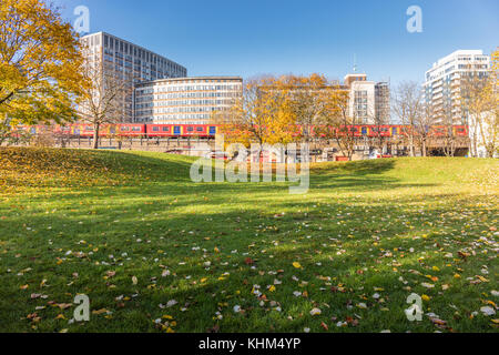 Vauxhall, Londra, Regno Unito; 17 novembre 2017; Autunno in scena a Vauxhall Pleasure Gardens. Alberi con foglie di giallo, un treno e edifici di uffici. Foto Stock