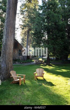 Due di legno sedie adirondack, vuota sotto un albero a breitenbush hot springs, adiacente al monte Cofano foresta nazionale nella città di montagna di Detroit, Oregon Foto Stock