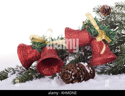Rosso campane di Natale e albero sempreverde succursale sulla neve con sfondo bianco Foto Stock