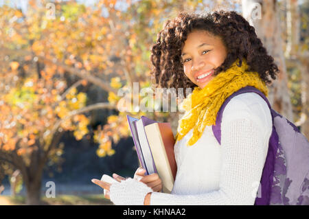 Attraente Africano nero studente americano in autunno con telefono azienda libri mentre sorridente alla fotocamera. Camera per copiare o testo. Foto Stock