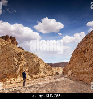 Senior uomo utilizzando il suo telefono per scattare fotografie presso il golden canyon, Death Valley, California, Stati Uniti d'America. Foto Stock