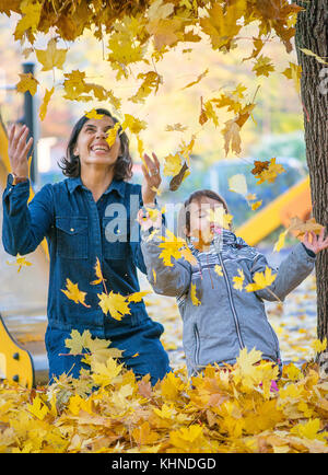 La madre e la sua piccola daugheter divertirsi nel parco con foglie Foto Stock