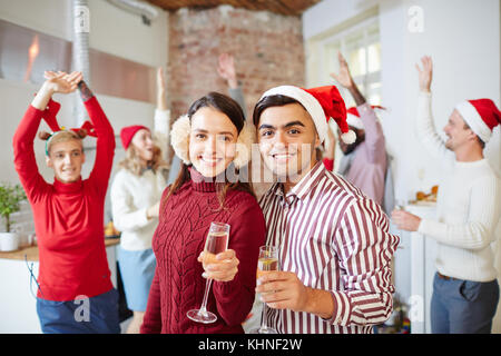 Felice ragazzo e ragazza con flauti di champagne osservando la fotocamera su sfondo di ballare gli amici Foto Stock