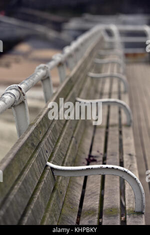 Un lungo antichi o vittoriano edwardian banco la prossima alla ringhiera a Cromer Pier in Norfolk. Posti a sedere presso il mare rastremantesi procedendo al di fuori della messa a fuoco a distanza. Foto Stock