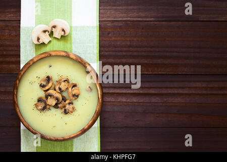 Mushroom cream soup guarnita con arrosti di fette di fungo cosparsi di pepe nero, servita nella ciotola di legno, fotografato tettuccio Foto Stock