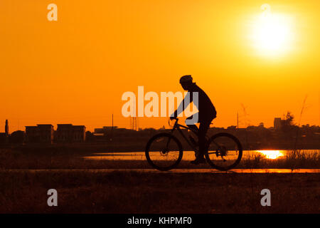 Silhouette sfocata gli uomini sono escursioni in bicicletta con sunrise,uomini esercitano la mattina sfocato di al di fuori della messa a fuoco Foto Stock