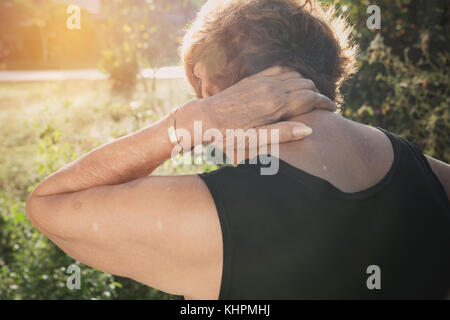 Vecchia donna che soffre di collo e muscolare problema problema all'aperto. Foto Stock