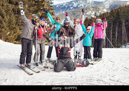 Il gruppo di un allegro amici in posa con sci e snowboardes sulla collina. guardando la fotocamera e divertirsi. Foto Stock