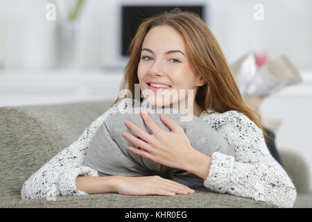 Felice giovane donna abbracciando un cuscino grigio Foto Stock