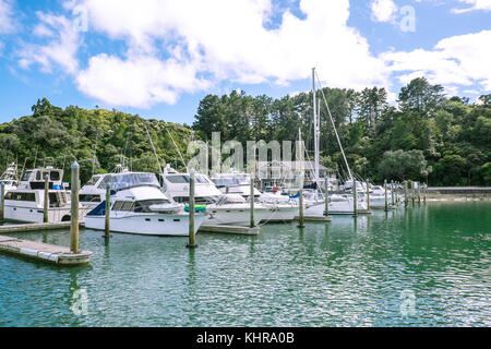 Barche a motore, yacht e lancia ormeggiati davanti a un edificio a Tutukaka Marina, Northland e North Island, Nuova Zelanda, NZ, con alberi e boccola in ba Foto Stock