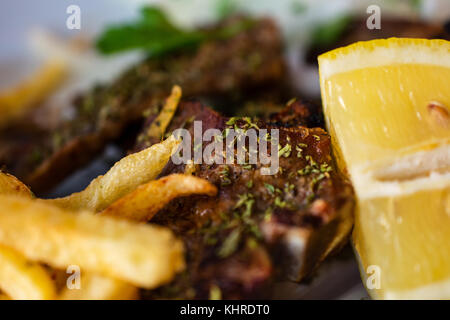 Serve deliziosi di piante succulente grigliate di grandi t-bone steak condita con erbe mediterranee accanto a patatine fritte e fetta di limone Foto Stock