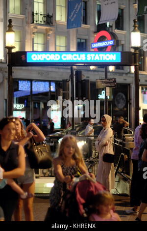 Donna in abito islamico sorge sul marciapiede mentre caucasian persone a piedi passato dalla stazione di Oxford Circus ingresso, Londra, Inghilterra Foto Stock