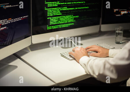 Inquadratura ravvicinata del programmatore irriconoscibile avvolto nella codifica mentre è seduto alla scrivania in ufficio Foto Stock