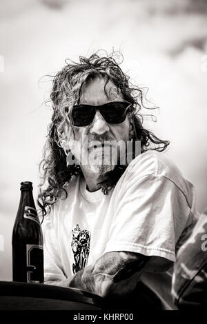 Con i capelli lunghi, tatuato uomo appoggiato su di un tavolo di fronte a una bottiglia di birra. Foto Stock