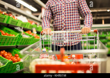 Vista frontale closeup dell uomo spingendo carrello con il cibo mentre l'acquisto di generi alimentari nel supermercato Foto Stock