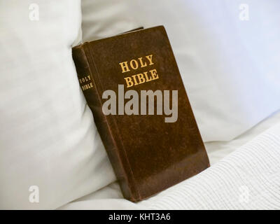 La Santa Bibbia libro posizionato sul letto con biancheria bianca e all'interno camera di albergo Foto Stock