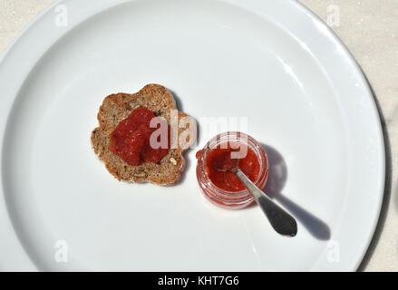 Pezzo di domestici, pane fatto in casa con cereali integrali e vaso piccolo con un delizioso wild confettura di fragole Foto Stock