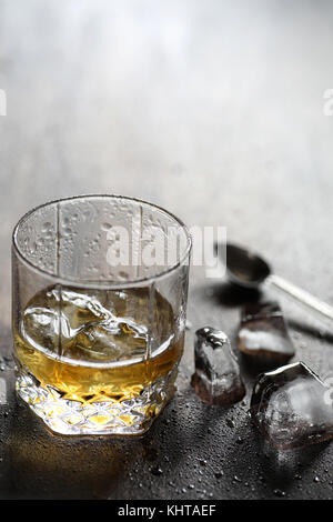 Whisky in un bicchiere e pezzi di ghiaccio su un legno Foto Stock