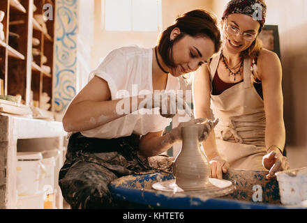 Donna al lavoro su potters ruota facendo una pentola di creta. Donna potter fare ritocchi alla pentola di creta sulla ruota di ceramiche. Foto Stock